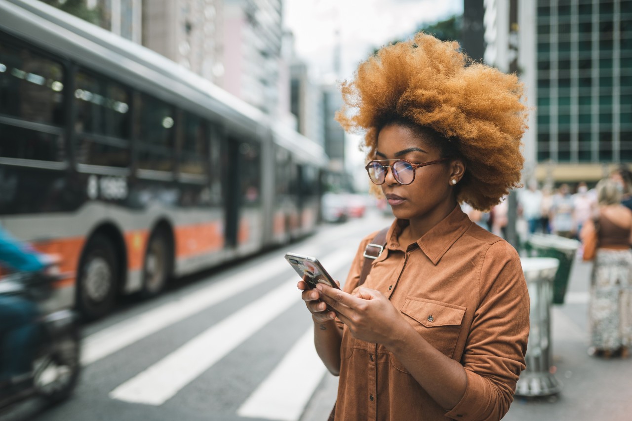 Mulher na rua com celular na mão