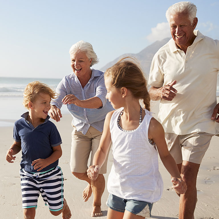 Grandparents running along beach with grandchildren on summer vacation
